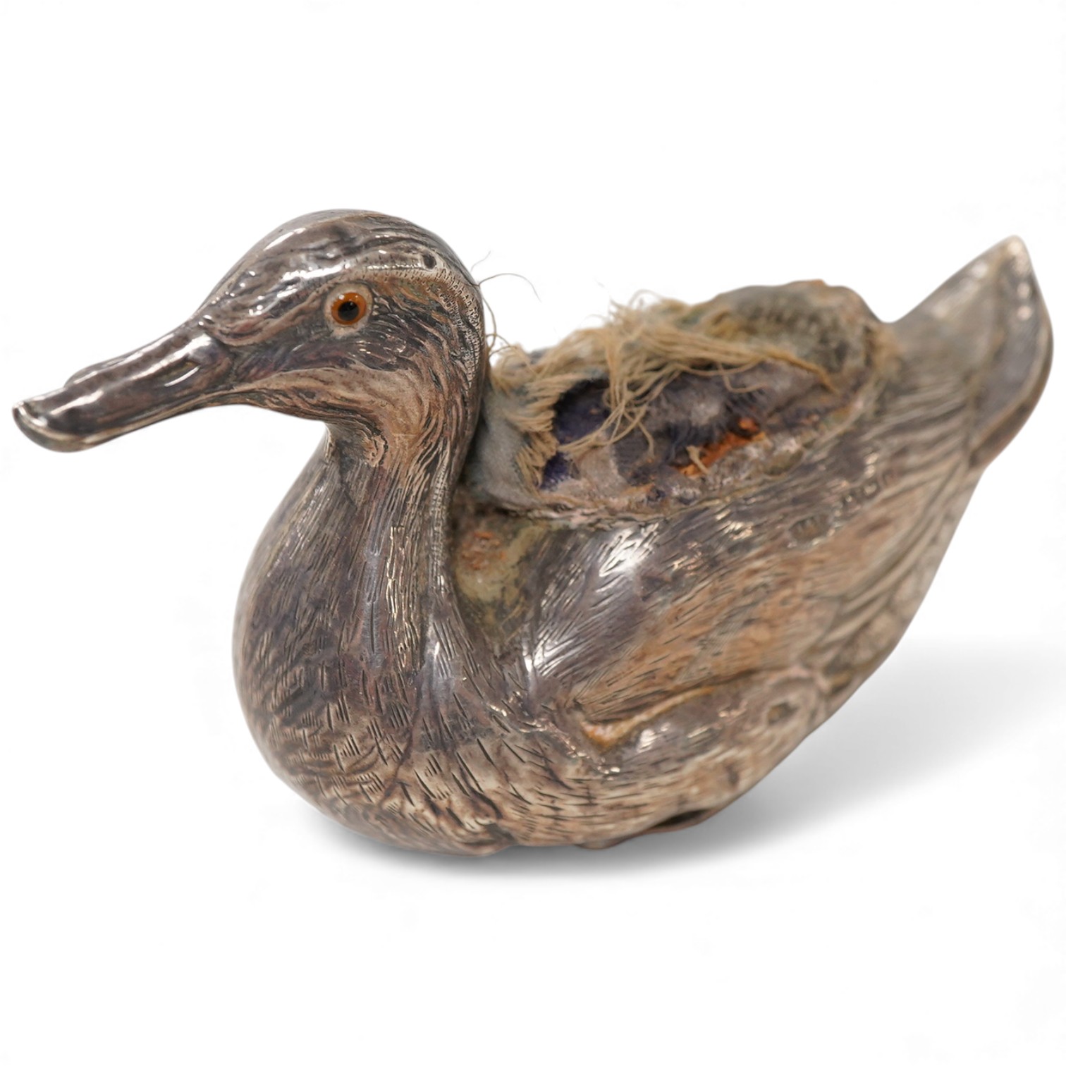 An Edwardian novelty silver mounted pin cushion, modelled as a duck, by Abrahall & Bint, engraved with 'feather' decoration and glass eyes, Birmingham, 1906, length 94mm, height 59mm(a.f.).